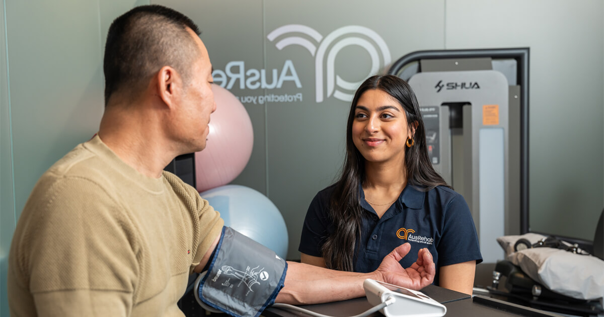 A man and woman seated in a room, using a blood pressure machine during AusRehab Pre-employment Screening Services