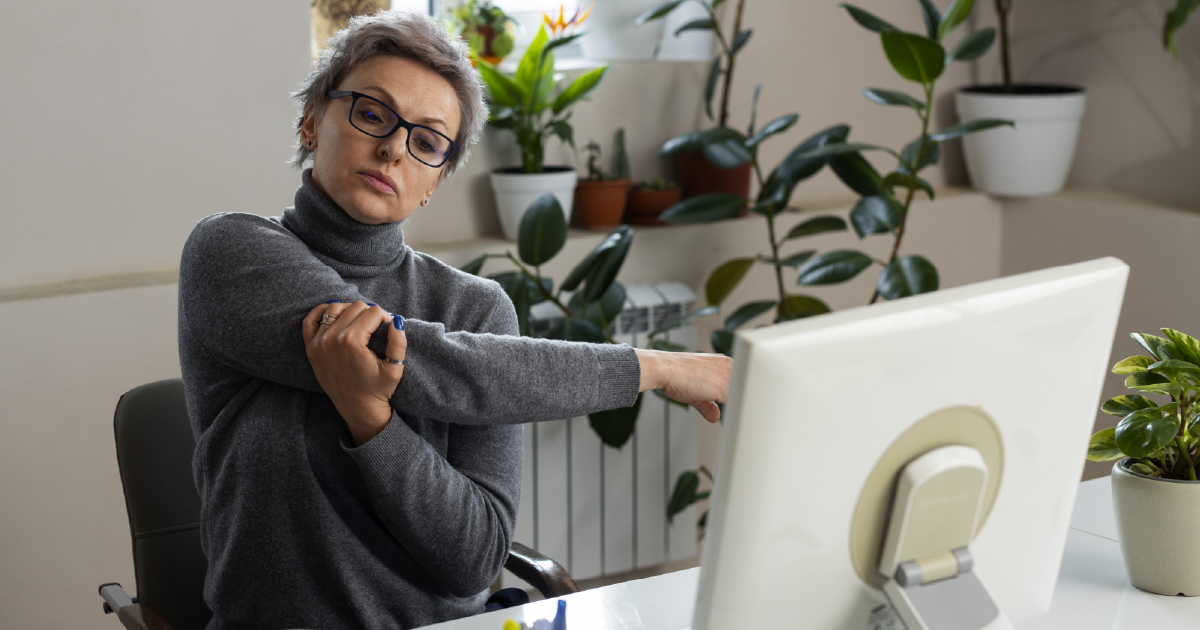 Office worker stretching arm at desk to prevent workplace injury, illustrating the benefits of ergonomic assessments for business health and productivity.